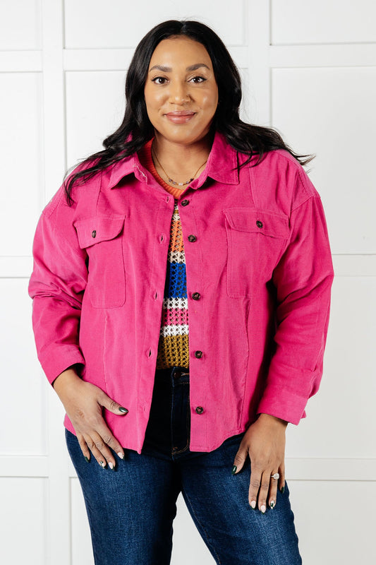 Woman wearing a bright pink jacket over a colorful shirt with a white background