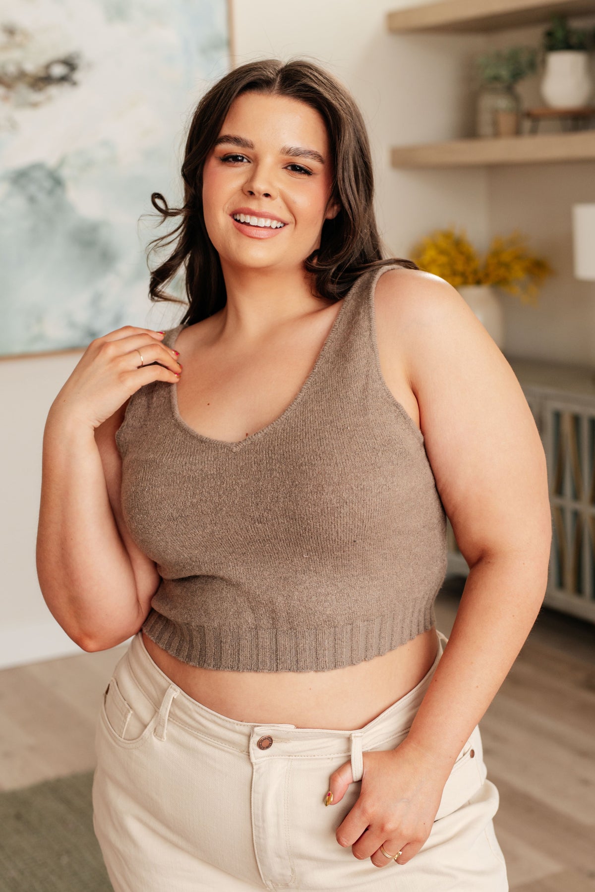 Woman wearing a brown knitted tank top and beige pants indoors.