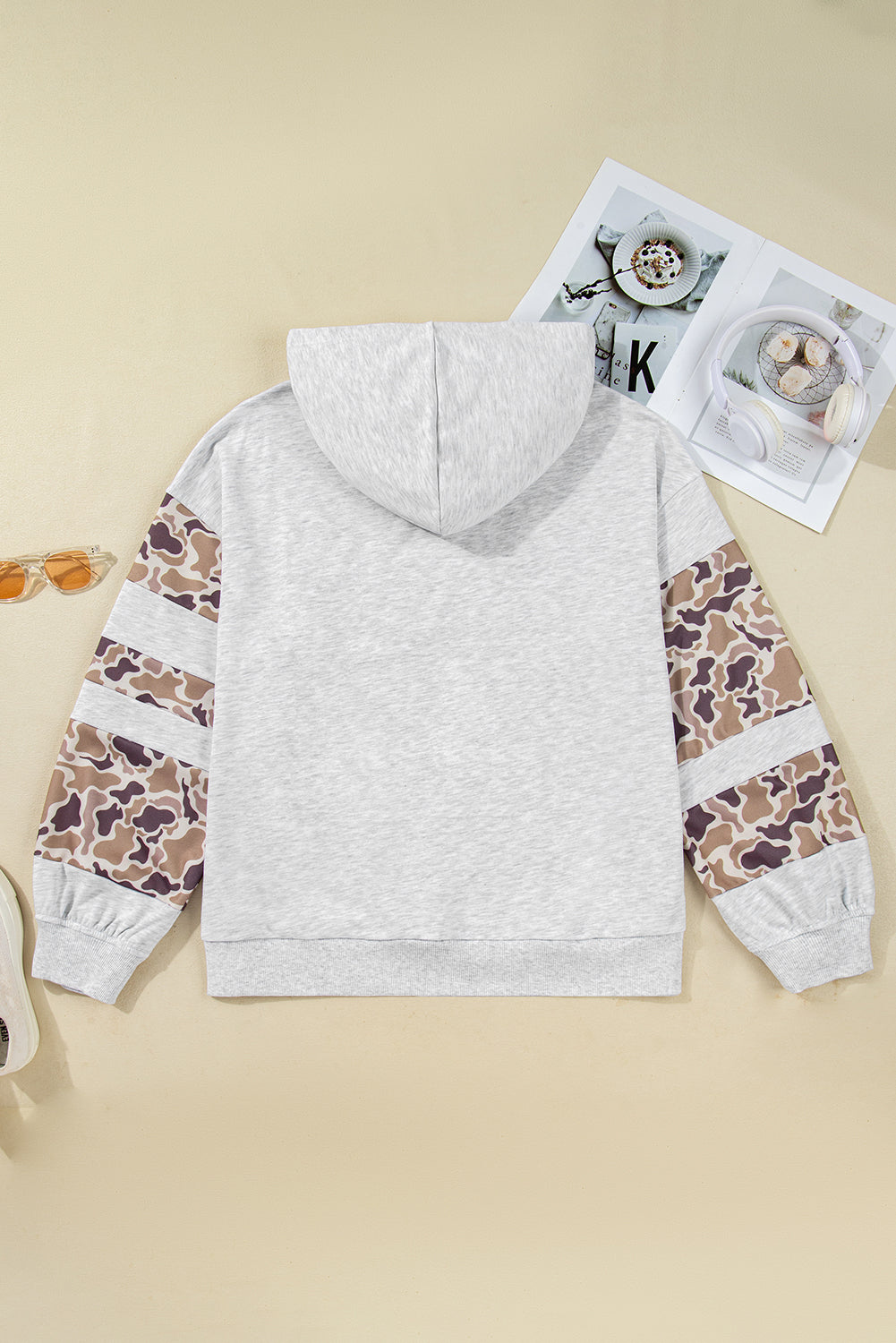 Gray hoodie with camouflage sleeves on a beige surface