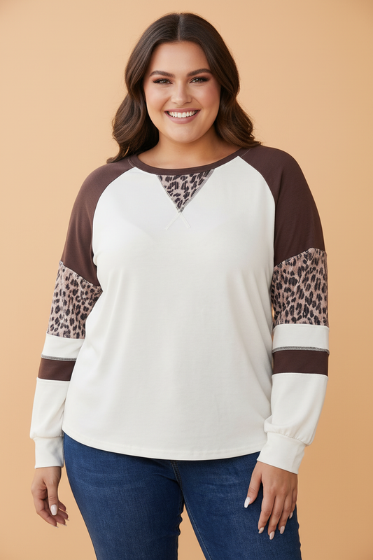 A woman modeling a long-sleeve raglan top with an off-white body, brown shoulder yoke, and leopard-print sleeve panels, paired with blue jeans against a solid beige background.