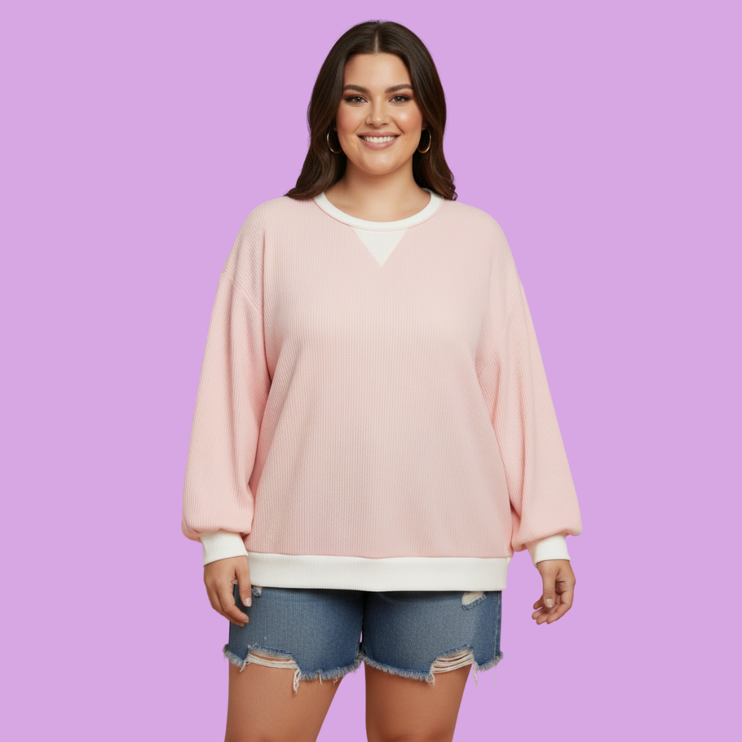 A woman modeling a light pink crewneck sweatshirt with white contrast trim, paired with distressed denim shorts, against a solid lavender background.