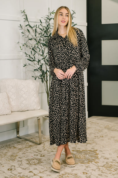 Woman wearing a black floral dress standing in a room with a white wall and decorative plant.