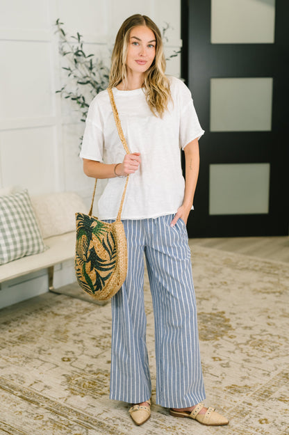 Woman holding a woven bag with a plant design in a room with a white wall and decorative elements.