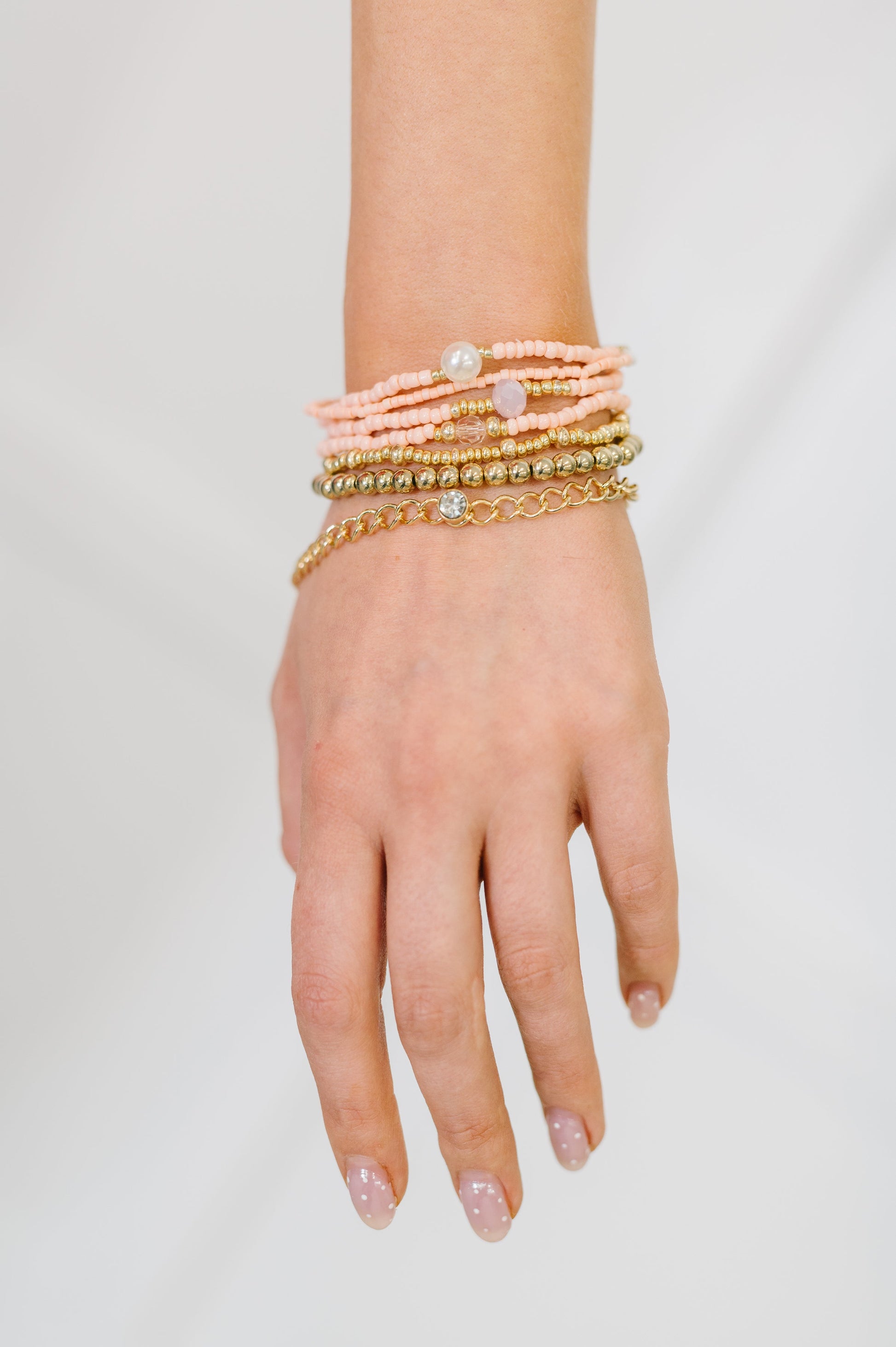 Hand wearing multiple bracelets on a plain background