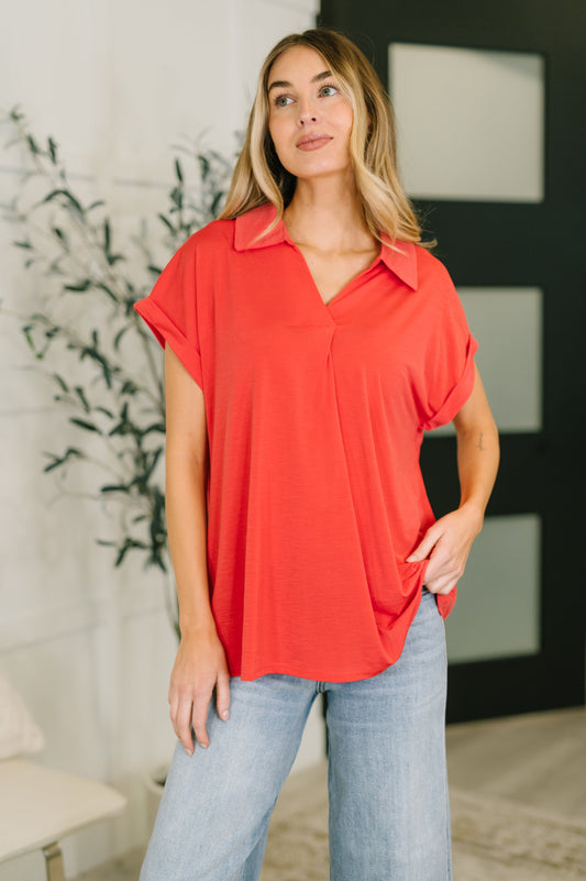 Woman wearing a red blouse and light blue jeans indoors.