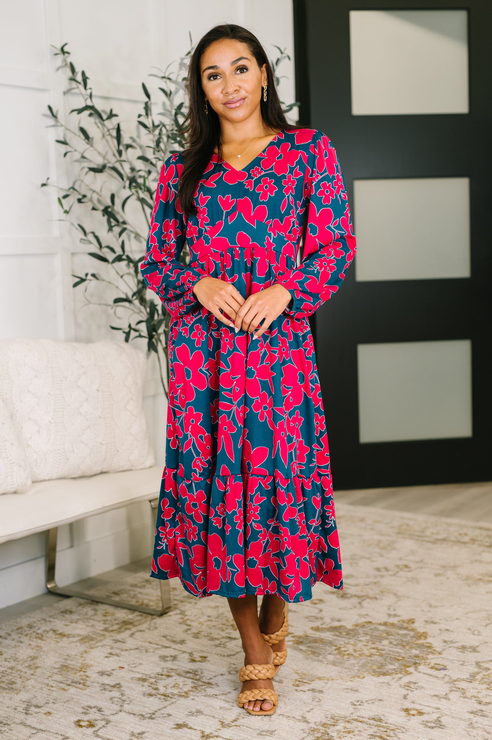 Woman wearing a floral dress in a room with a plant and white wall.
