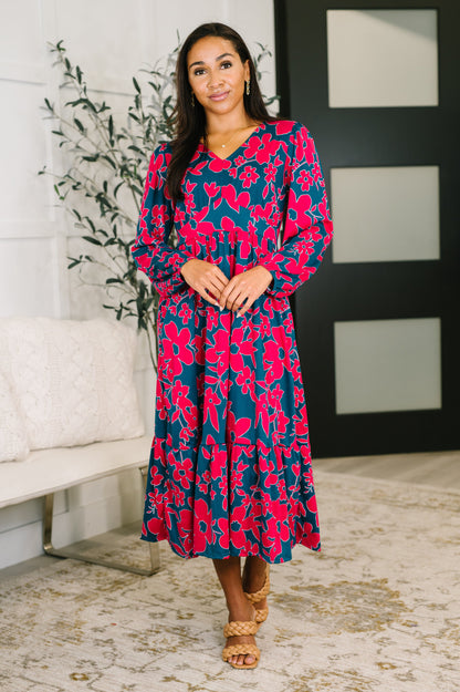Woman wearing a floral dress in a room with a plant and white wall.