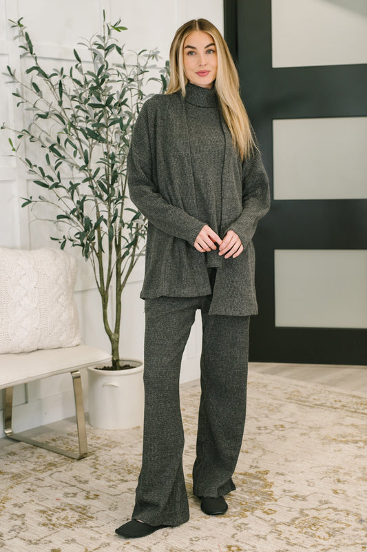 Woman wearing a gray outfit standing in a room with a plant and white wall.