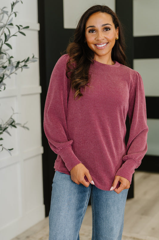Woman wearing a maroon ribbed sweater and blue jeans indoors.