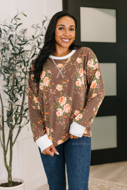 Woman wearing a floral long-sleeve top and jeans indoors with a plant in the background