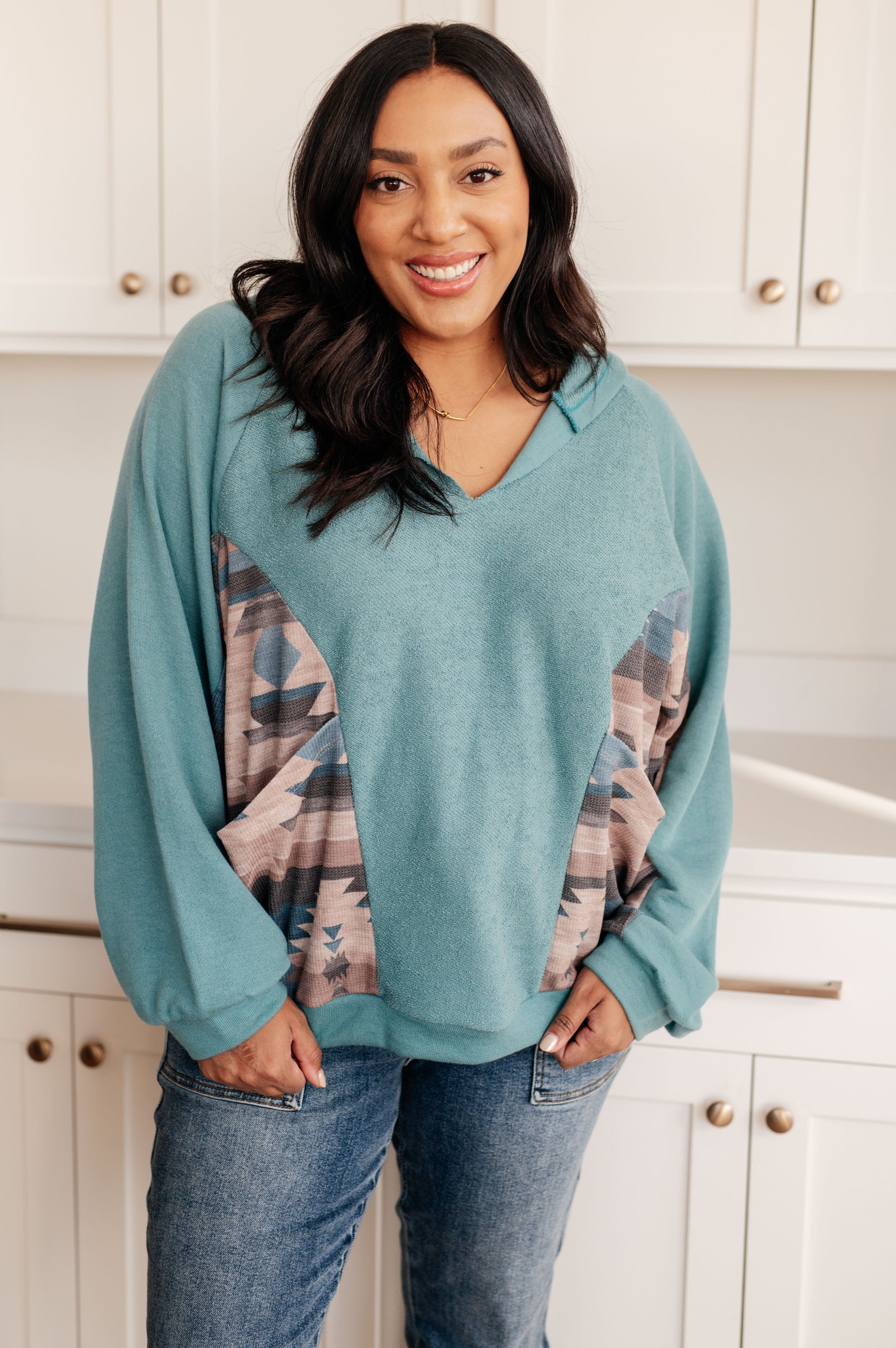 Woman wearing a teal sweater with plaid sleeves in a kitchen setting