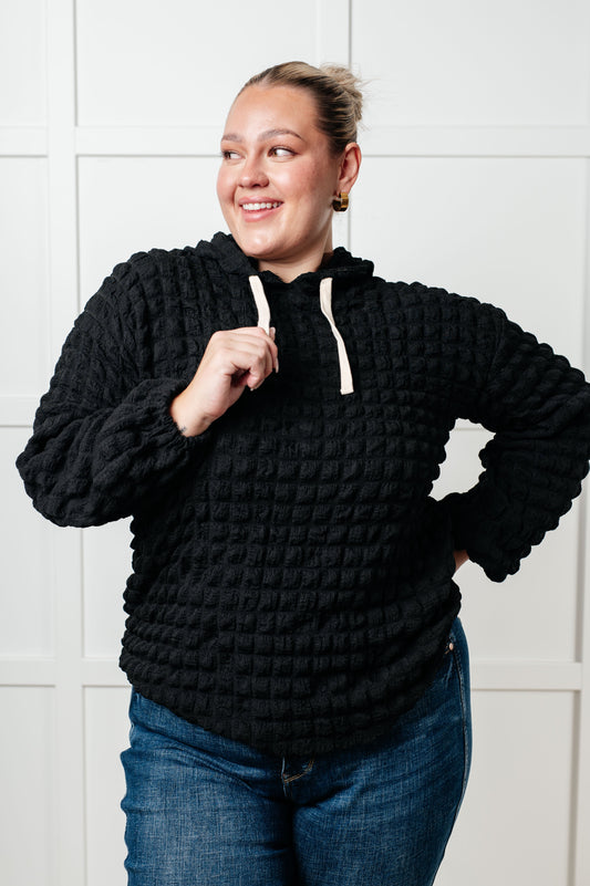 Person wearing a black textured hoodie with a white tiled wall background