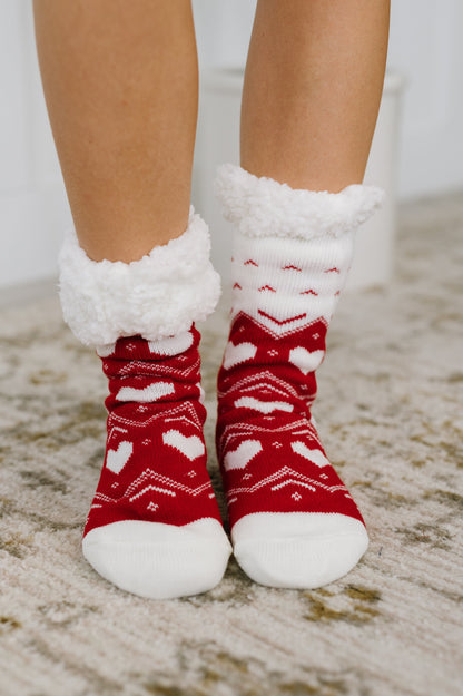 Red and white patterned socks with fluffy cuffs worn on a carpeted floor.