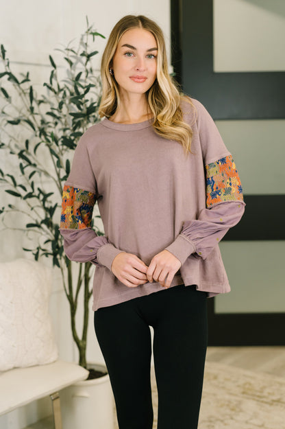 Woman wearing a mauve long-sleeve top with floral cuffs in a home setting