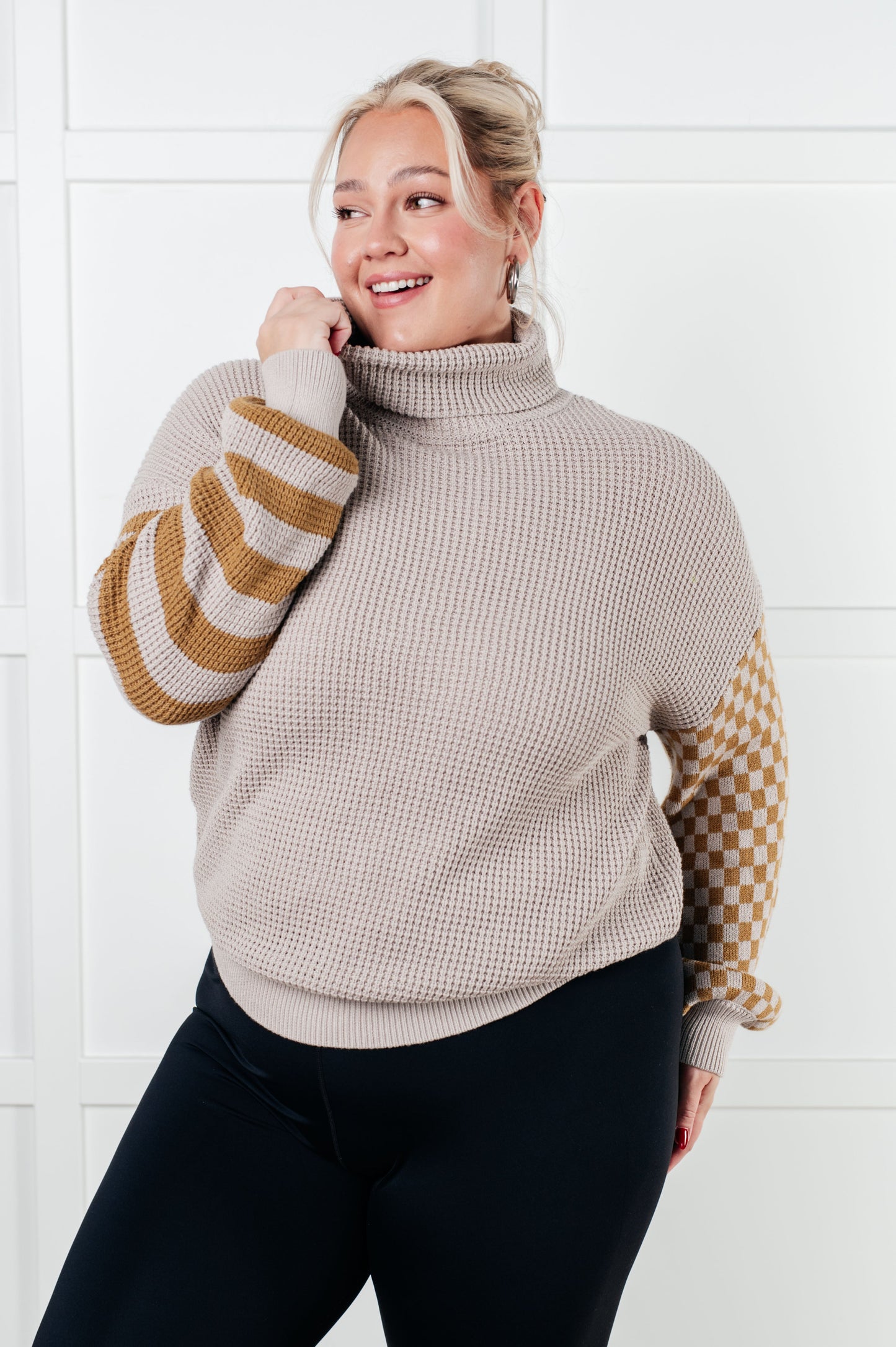 Woman wearing a beige turtleneck sweater with patterned sleeves against a white background