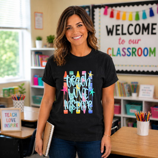 Teacher wearing Teach Love Inspire Crayon Graphic Tee on Gildan Softstyle Black with colorful crayon design in a classroom setting.
