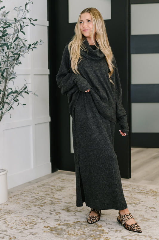 Woman wearing a long dark gray sweater dress standing indoors.