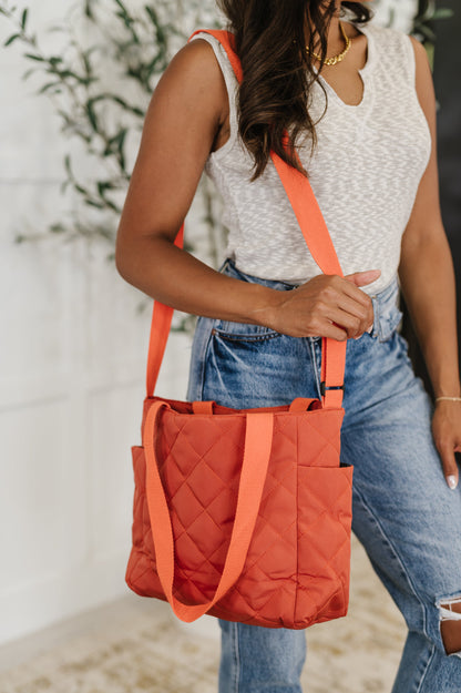 Woman holding an orange quilted handbag with a blurred background