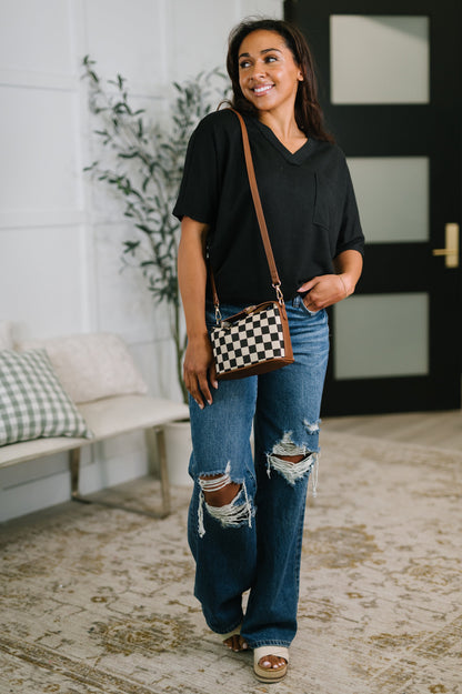 Woman wearing a black shirt and ripped jeans, holding a checkered bag indoors.