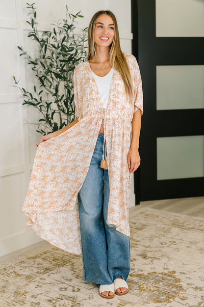 Woman wearing a long, light-colored kimono-style garment with blue jeans indoors.