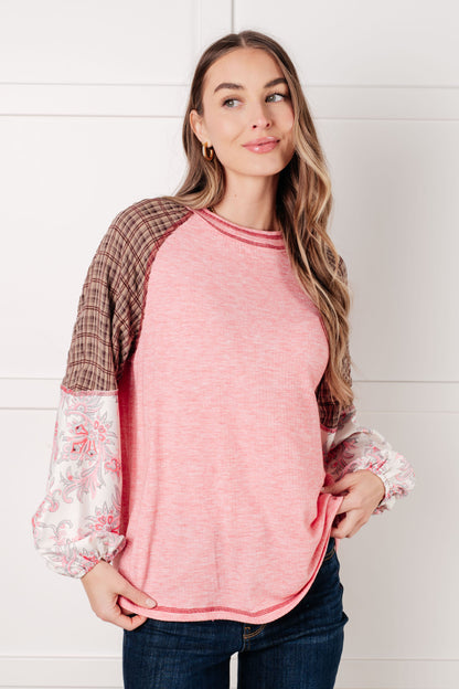 Woman wearing a pink long-sleeve top with plaid and lace details against a white background