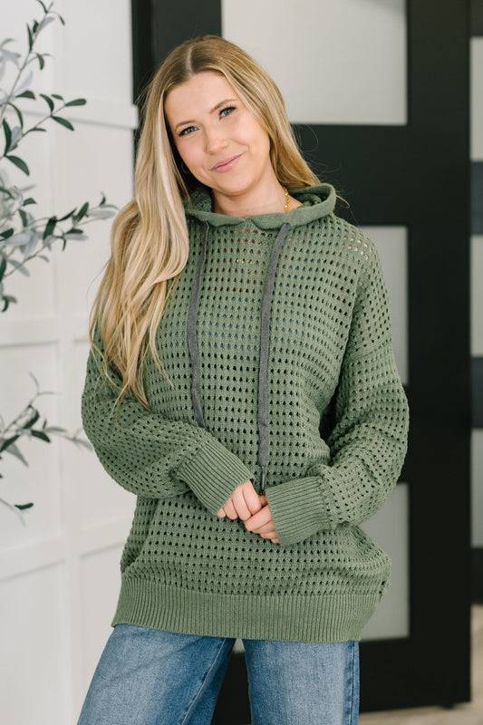 Woman wearing a green crochet hoodie with a blurred indoor background