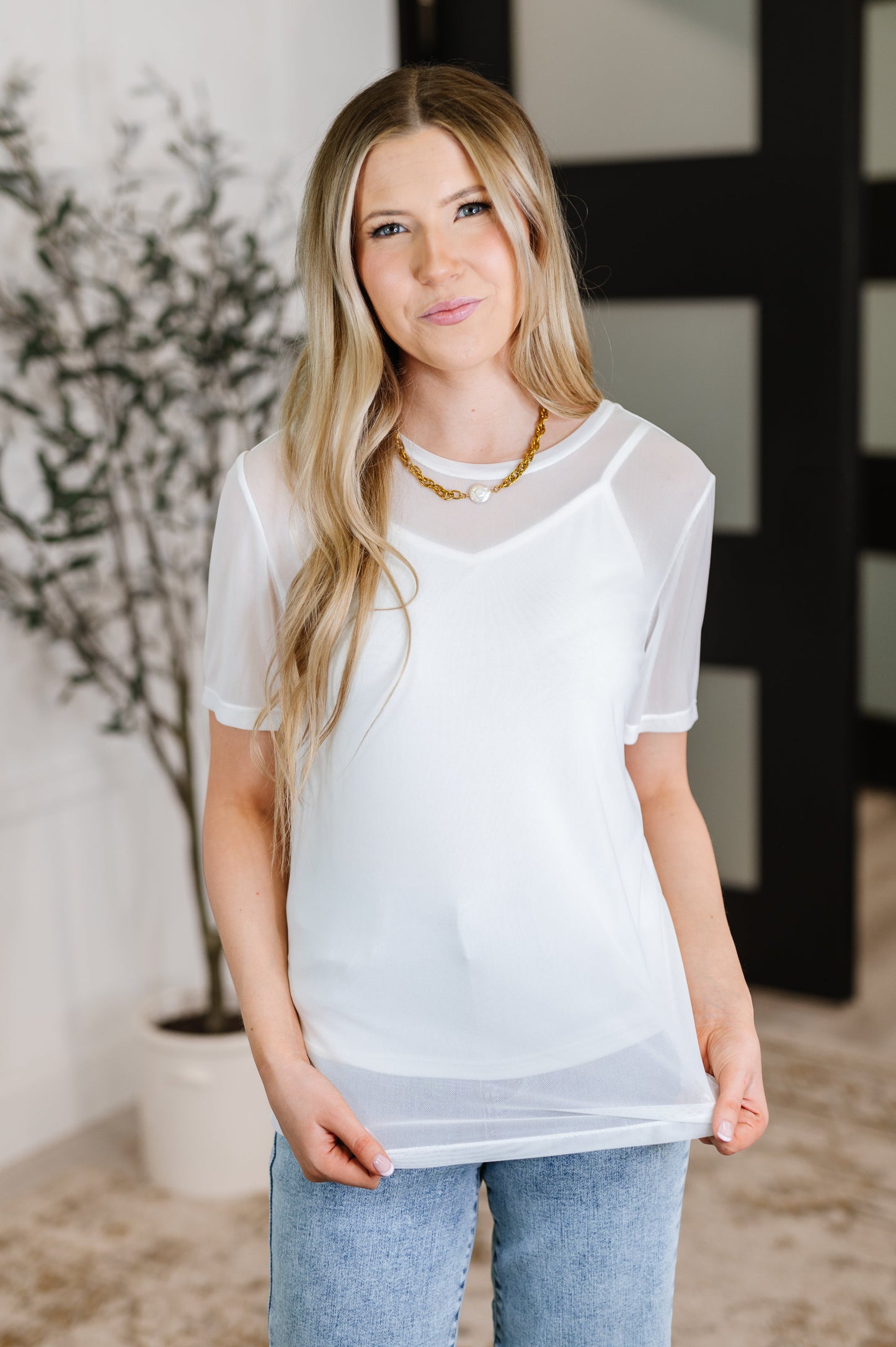 Woman wearing a sheer white top with a blurred indoor background