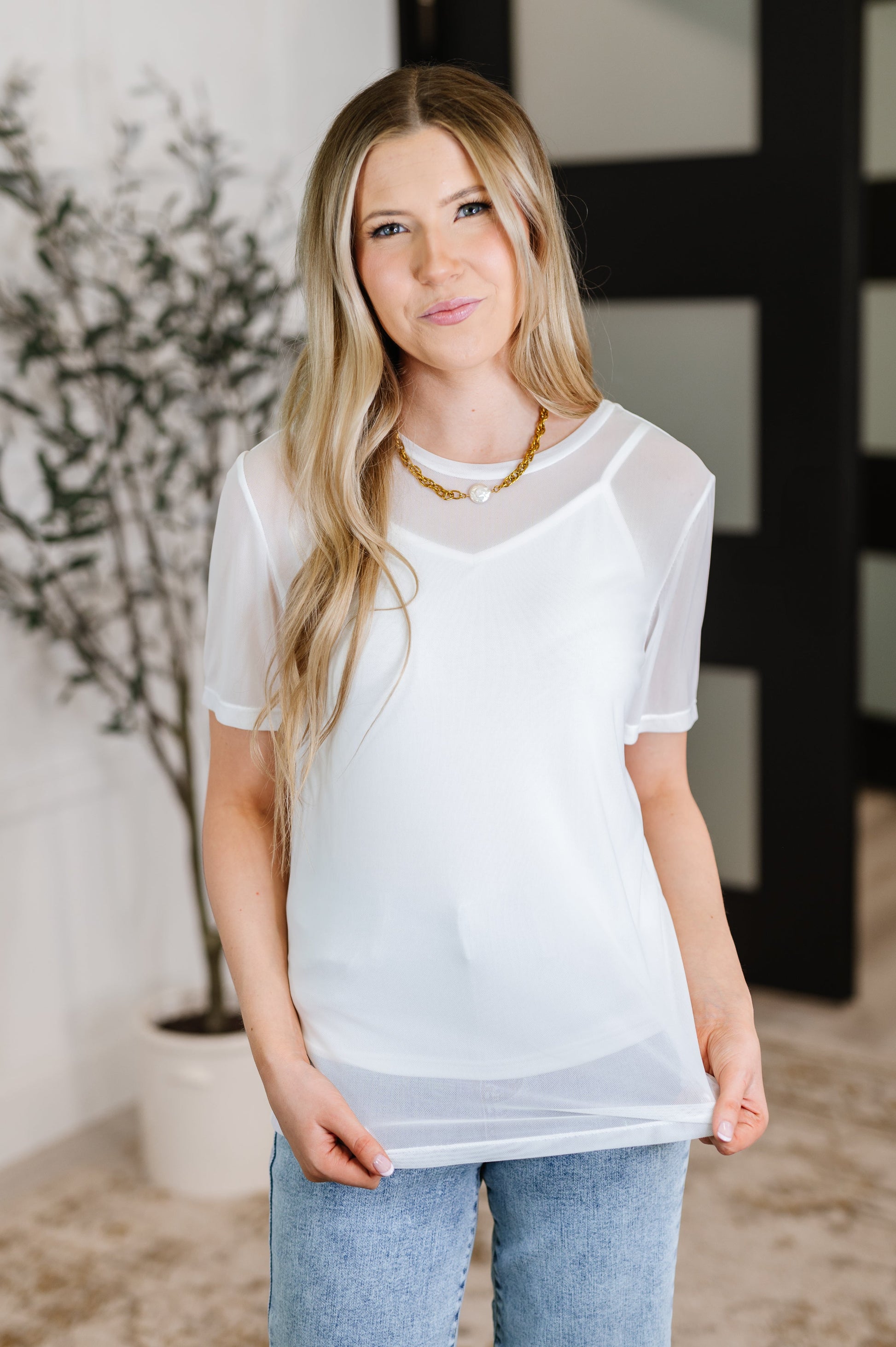 Woman wearing a sheer white top with a blurred indoor background