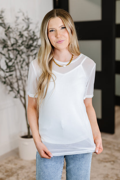 Woman wearing a sheer white top with a blurred indoor background