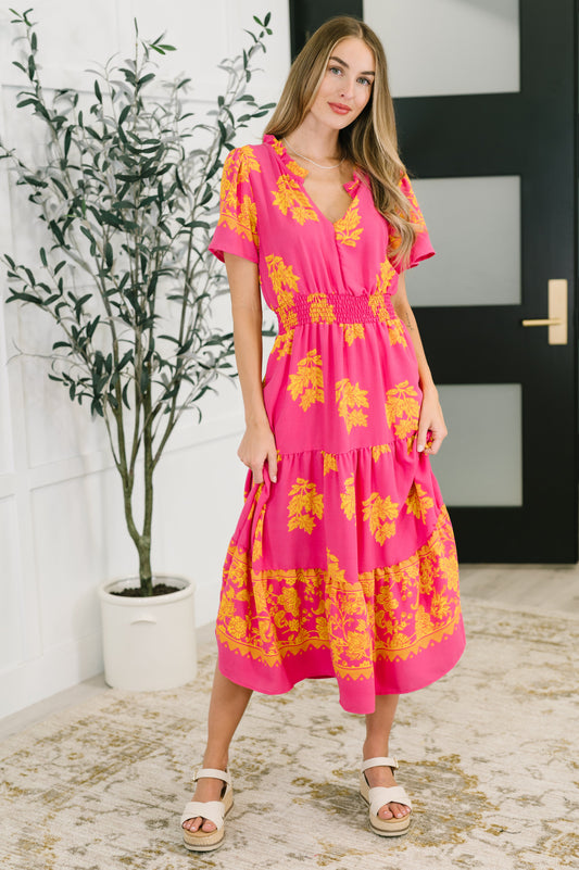 Woman wearing a pink floral dress standing indoors with a plant in the background