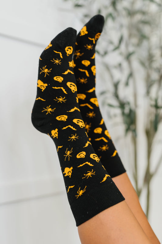 Black socks with yellow spider pattern held against a neutral background