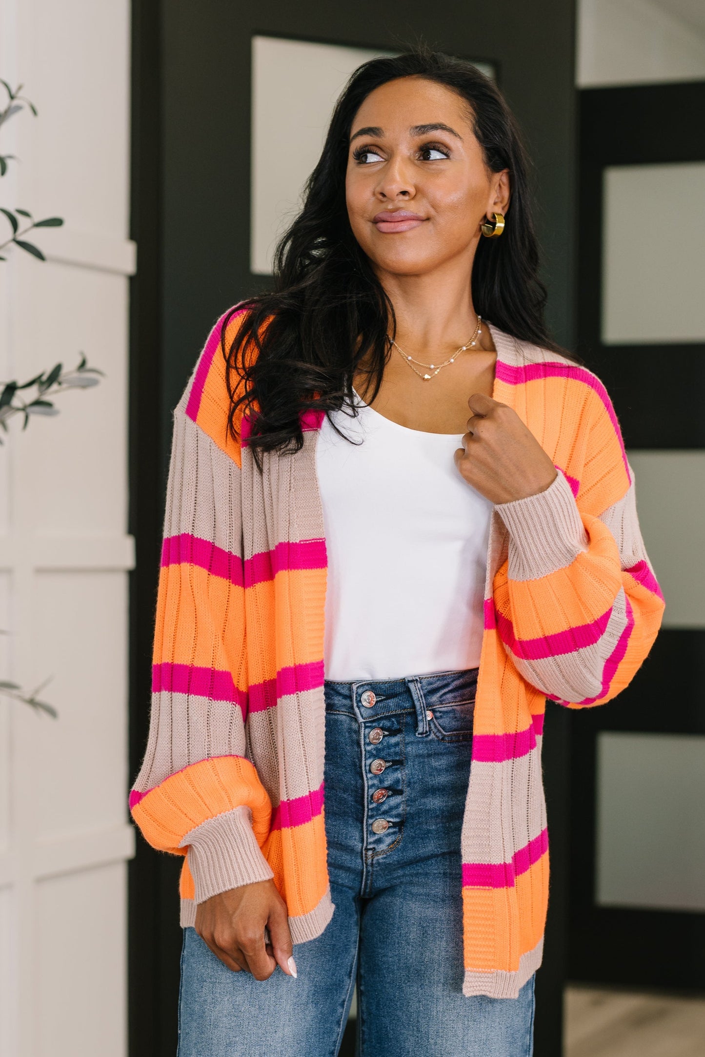 Woman wearing a colorful striped cardigan with a white top and blue jeans.